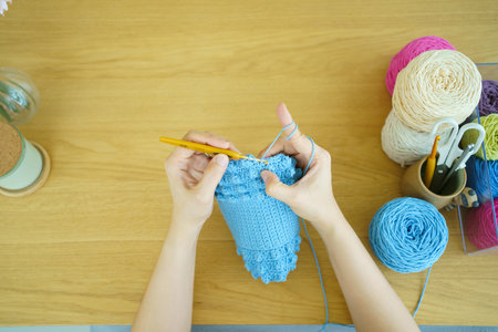 Happy cheerful Asian woman doing a crochet in living room in free time. Skillful Asian craftswoman knitting a handcraft crochet sweater and hat in cozy living room.の写真素材