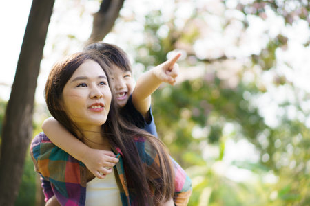 Asian woman and boy playing and walking around the park together with beautiful bokeh and lighting background copyspace. Little cute boy hogging his mother from back and kissing.の写真素材