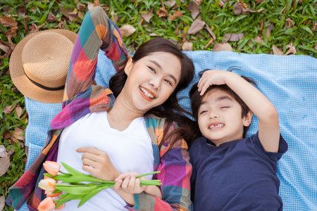 Lovely cute Asian little boy laying down on the grass field with his mother, boy and mother relaxing - sleeping during the day in backyard garden.の写真素材