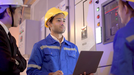 Professional electrical engineer team using laptop computer to inspecting the electrical circuit in control room. Team of electrical engineers having a discussion together about system maintenance.の写真素材