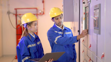 Professional electrical engineer team using laptop computer to inspecting the electrical circuit in control room. Team of electrical engineers having a discussion together about system maintenance.の写真素材