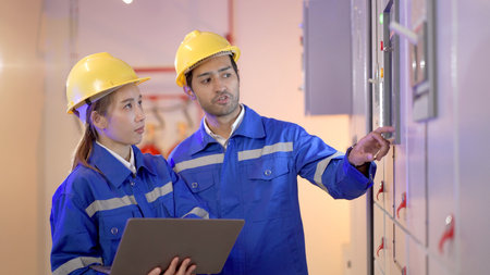 Professional electrical engineer team using laptop computer to inspecting the electrical circuit in control room. Team of electrical engineers having a discussion together about system maintenance.の写真素材
