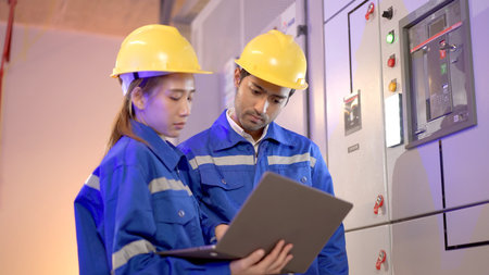 Professional electrical engineer team using laptop computer to inspecting the electrical circuit in control room. Team of electrical engineers having a discussion together about system maintenance.の写真素材