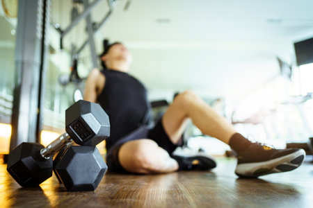 Happy cheerful Asian sportsman relaxing - sitting on the floor after done a weight training exercise in an indoor fitness or gym. Man resting after did a wight training workout.の写真素材