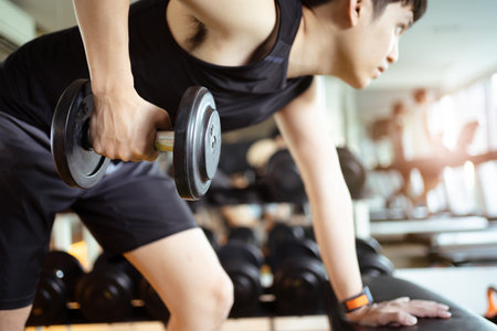 Active Asian sportsman doing a weight training exercise by lifting up a dumbbell, man lifting up or holding a heavy dumbbell in Overhead Tricep Extension position. Bodybuilding workout.の写真素材
