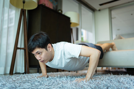 Happy Asian strong sportsman making an exercise at home in living room, man doing a body weight...