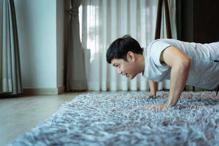 Happy Asian strong sportsman making an exercise at home in living room, man doing a body weight training workout by push up on the floor.の写真素材