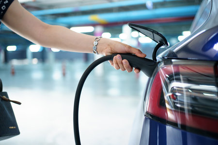Beautiful Asian woman connecting a AC Type 2 EV charging connector to a vehicle, woman preparing an EV - electric vehicle charging connector for recharge a vehicle.の写真素材