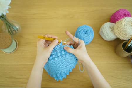 Happy cheerful Asian woman doing a crochet in living room in free time. Skillful Asian craftswoman knitting a handcraft crochet sweater and hat in cozy living room.の写真素材