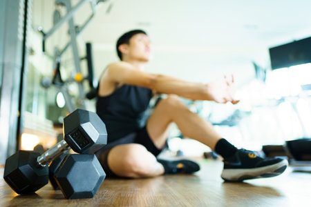 Happy cheerful Asian sportsman relaxing - sitting on the floor after done a weight training exercise in an indoor fitness or gym. Man resting after did a wight training workout.の写真素材