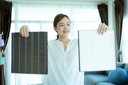 Asian woman changing the dirty air purifier filter after using for a long time in the dirty air environment. Using air purifier clean the air for better atmosphere in a house.の写真素材