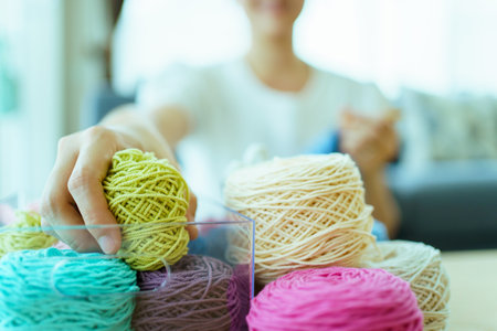 Happy cheerful Asian woman doing a crochet in living room in free time. Skillful Asian craftswoman knitting a handcraft crochet sweater and hat in cozy living room.の写真素材