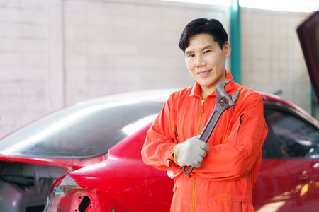 Automobile technician working in auto garage, professional Asian male automotive technician smiling to camera while fixing - repairing a vehicle in garage close up.の写真素材