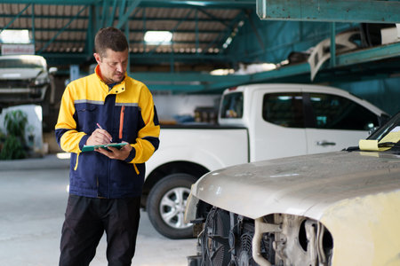 Senior professional automotive technician inspecting the damaged vehicle in garage. Car mechanical engineer or technician inspecting and checking surrounding the car before fixing.の写真素材