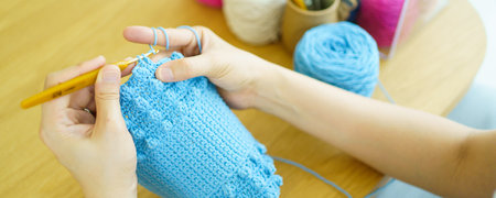 Happy cheerful Asian woman doing a crochet in living room in free time. Skillful Asian craftswoman knitting a handcraft crochet sweater and hat in cozy living room.の写真素材