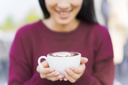 Beautiful Asian young woman holding a coffee cup on a hands close up. Woman enjoy drinking a coffee in morining with breakfast.の写真素材