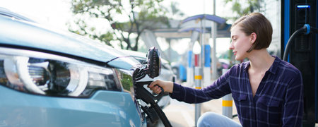 Happy beautiful caucasian white woman driver preparing to recharge her electric vehicle or EV car at EV fast charge station during the trip. Future and sustainable transportation concept.の写真素材