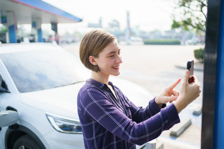 beautiful; caucasian white woman driver preparing to recharge her electric vehicle or EV car at EV fast charge station during the trip. Future and sustainable transportation concept.の写真素材