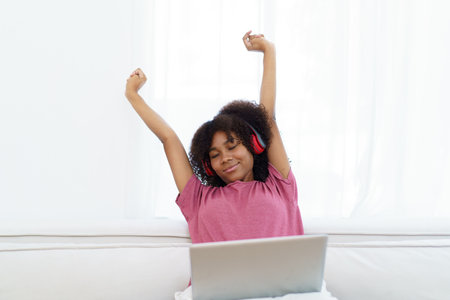 American - African black young woman sitting on sofa in living room and enjoy watching a social media on laptop computer in free time.の写真素材