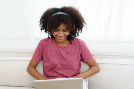 American - African black young woman sitting on sofa in living room and enjoy watching a social media on laptop computer in free time.の写真素材