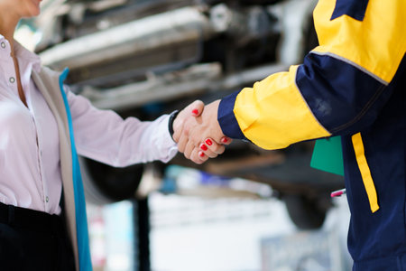 Caucasian white young woman taking her car to garage to have an annual check up and talking or discussing to technician. Automobile repairing and diagnostics service business concept.の写真素材