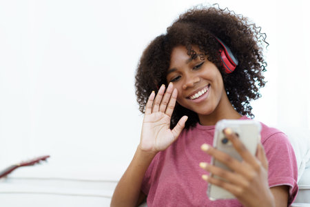 Happy cheerful American - African black teenager woman relaxing in the living room and using smartphone to browse the social network or internet. Woman relaxing in living room and using smartphone.の写真素材