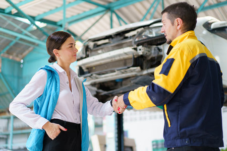 Caucasian white young woman taking her car to garage to have an annual check up and talking or discussing to technician. Automobile repairing and diagnostics service business concept.の写真素材