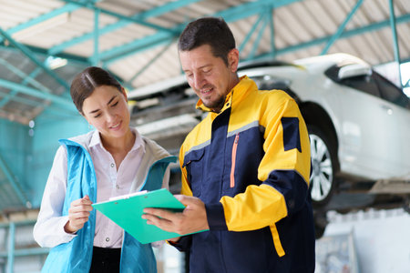 Caucasian white young woman taking her car to garage to have an annual check up and talking or discussing to technician. Automobile repairing and diagnostics service business concept.の写真素材