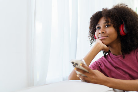 Happy cheerful American - African black teenager woman relaxing in the living room and using smartphone to browse the social network or internet. Woman relaxing in living room and using smartphone.の写真素材