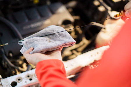 Senior Asian man checking or measuring a vehicle oil engine or engine lubricant level by using oil stick indicator. Senior professional repairman inspecting an oil engine in an old car.の写真素材