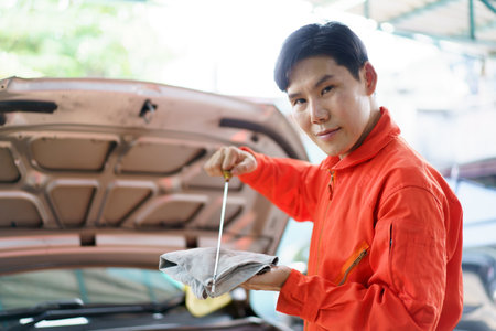 Senior Asian man checking or measuring a vehicle oil engine or engine lubricant level by using oil stick indicator. Senior professional repairman inspecting an oil engine in an old car.の写真素材