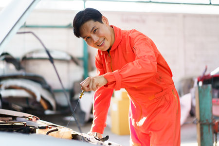 Senior Asian man checking or measuring a vehicle oil engine or engine lubricant level by using oil stick indicator. Senior professional repairman inspecting an oil engine in an old car.の写真素材