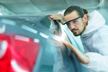 Professional automotive painting technician in chemical protecting suit inspecting car painting quality in painting chamber together. Car painting and detailing technicians portrait.の写真素材