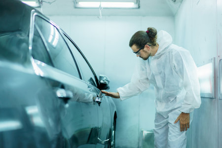 Professional automotive painting technician in chemical protecting suit inspecting car painting quality in painting chamber together. Car painting and detailing technicians portrait.の写真素材