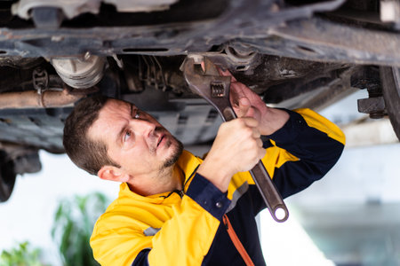 Professional caucasian white automobile technician inspecting and checking under - suspension of a vehicle  in garage.の写真素材
