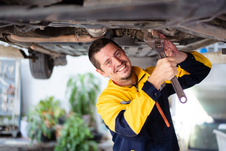 Professional caucasian white automobile technician inspecting and checking under - suspension of a vehicle  in garage.の写真素材