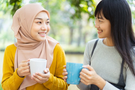 Happy beautiful Asian Muslim women and friend relaxing - having a meal together in a park, different or diverse religious friends concept.の写真素材
