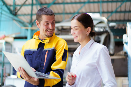 Young caucasian white woman taking technician in garage about vehicla annual check up - maintenance.の写真素材