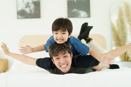 Happy Asian people family, a lovely little young boy playing with father in bedroom together. Father and son playing in bedroom.の写真素材