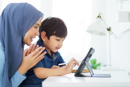 Happy cheerful Asian muslim woman woman teaching her little son a drawing on digital tablet, mother let her little young boy doing a school homework or an online learning on tablet.の写真素材