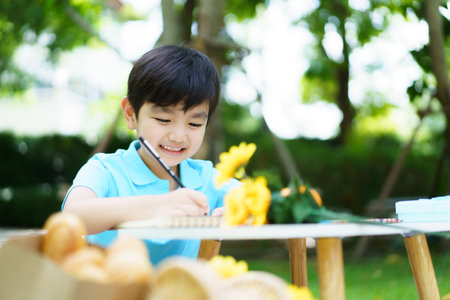 Happy cheerful Asian little boy enjoy drawing and painting alone at home backyard alone, boy drawing a picture at outdoor garden portrait on a beautiful natural bokeh background.の写真素材