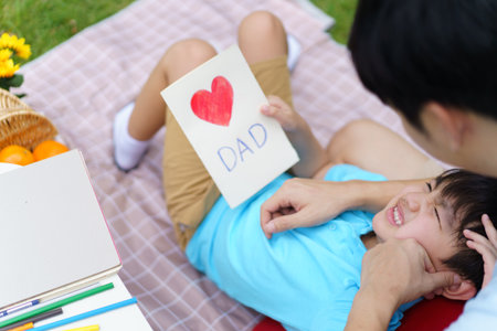 Lovely Asian little young boy giving his daddy the greeting card for the international father's day, lovely boy gives his father a drawing DIY Father's Day greeting card.の写真素材