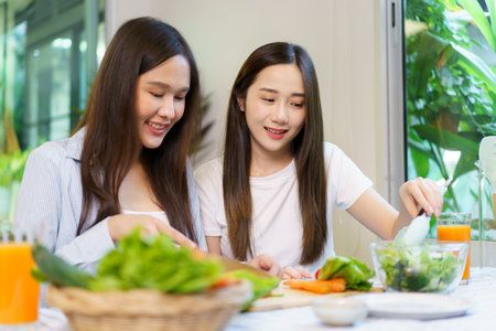 Asian women enjoying eating a breakfast and drinking organic orange juice together in the dining room. Cute Asian women cheering an orange juice in a glass together.の写真素材