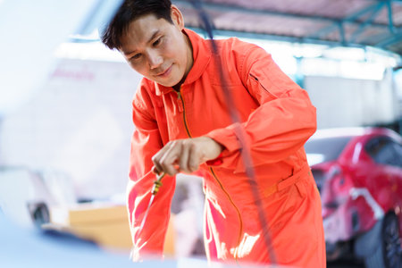 Senior Asian man checking or measuring a vehicle oil engine or engine lubricant level by using oil stick indicator. Senior professional repairman inspecting an oil engine in an old car.の写真素材