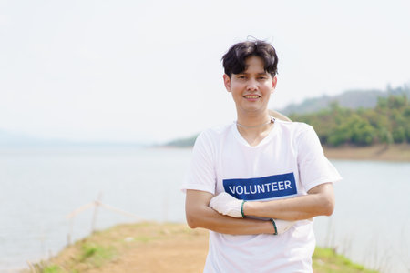 Handsome Asian volunteer smiling to camera portrait, man pointing finger at his volunteer t-shirt. Happy cheerful male volunteer proudly smiles to camera while working.の写真素材