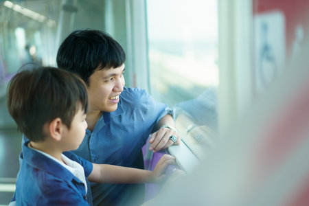 Happy cheerful Asian father and son traveling in the city on the sky train, man taking his lovely...