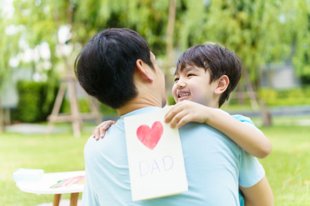 Lovely Asian little young boy giving his daddy the greeting card for the international father's day, lovely boy gives his father a drawing DIY Father's Day greeting card.の写真素材
