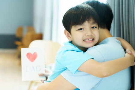 Lovely Asian little young boy giving his daddy the greeting card for the international father's day, lovely boy gives his father a drawing DIY Father's Day greeting card.の写真素材