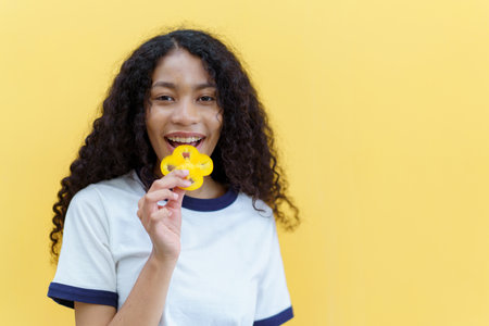 Happy cheerful American - African black woman holding a sliced piece of the yellow bell pepper and smile close up with copyspace on bright yellow background.の写真素材