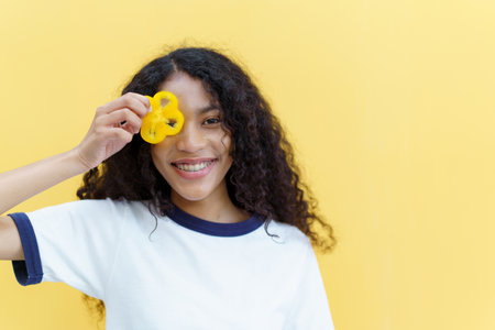 Happy cheerful American - African black woman holding a sliced piece of the yellow bell pepper and smile close up with copyspace on bright yellow background.の写真素材